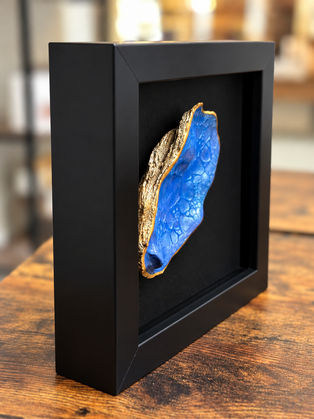 Side view of framed blue oyster shell artwork showing gold edges and dimensional shadow box