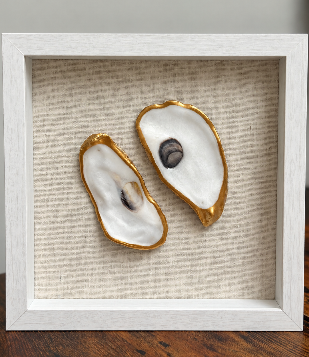 Two natural oyster shells with gold edges in a 9x9 whitewashed shadow box with linen background